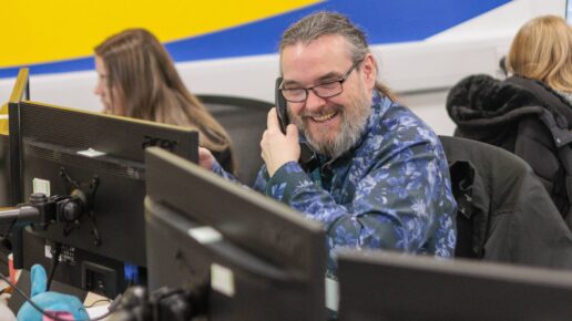 An image of a man at a desk in an office environment, answering a phone call.