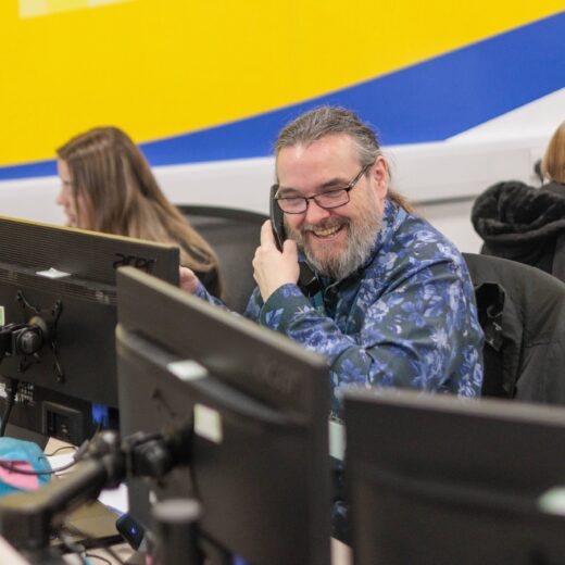 An image of a man at a desk in an office environment, answering a phone call.
