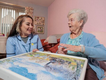Image of a Care Assistant and an elderly lady, sat on a couch whilst playing a jigsaw puzzle.