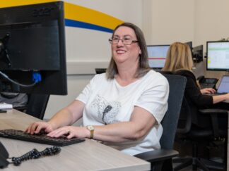 An image of a woman at a desk in an office environment, answering a phone call.