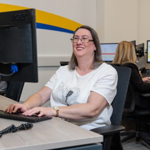 An image of a woman at a desk in an office environment, answering a phone call.