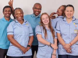 A group of 5 Care Assistants against a white wall.