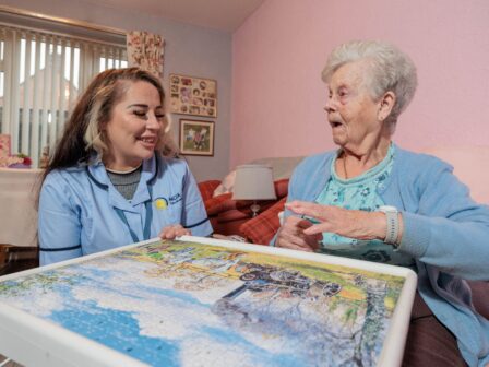 Image of a Care Assistant and an elderly lady, sat on a couch whilst playing a jigsaw puzzle.