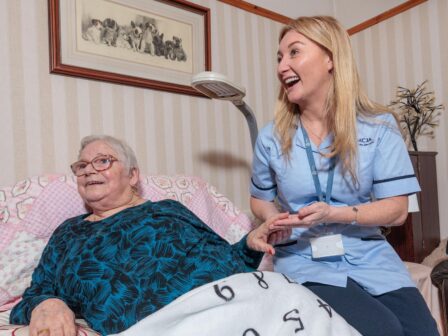 Image of a Care Assistant and an elderly lady in a home setting, holding hands.