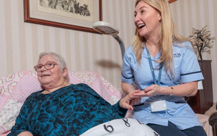 Image of a Care Assistant and an elderly lady in a home setting, holding hands.