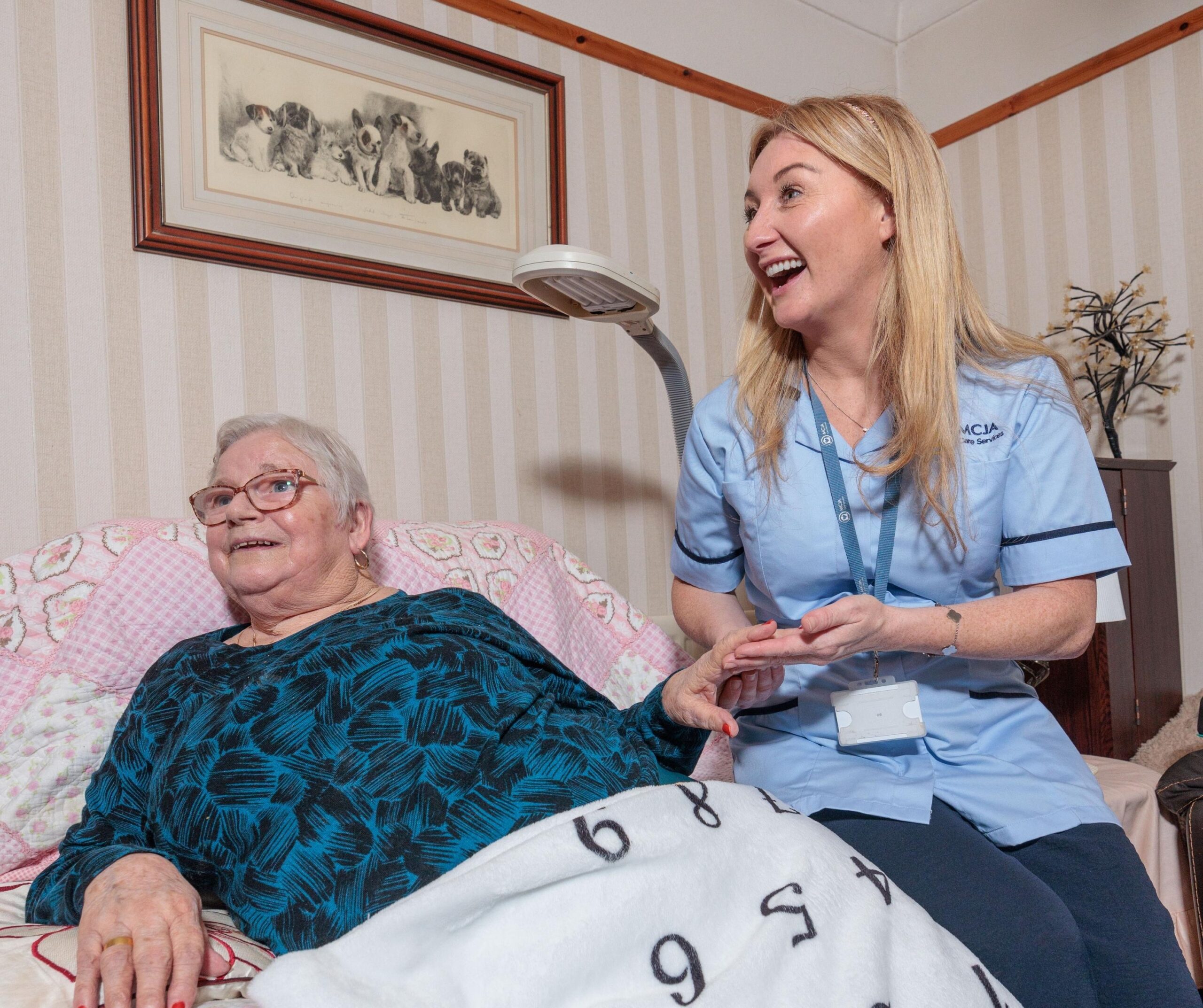 Image of a Care Assistant and an elderly lady in a home setting, holding hands.