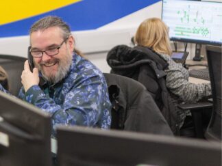 An image of a man at a desk in an office environment, laughing whilst answering a phone call.