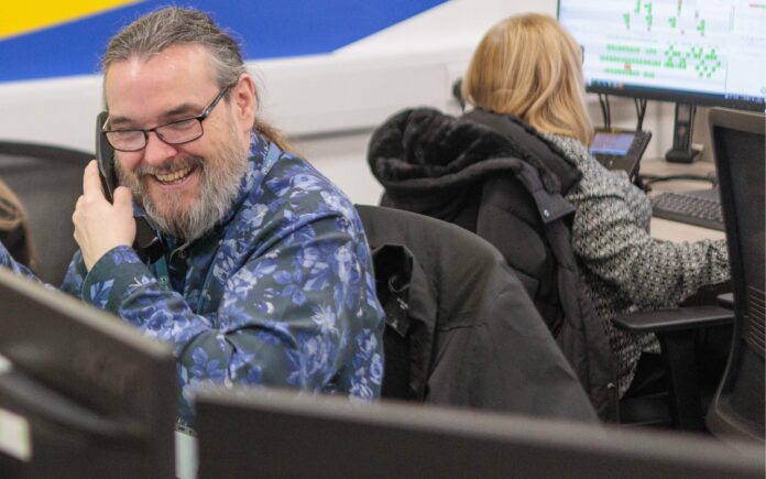 An image of a man at a desk in an office environment, answering a phone call.