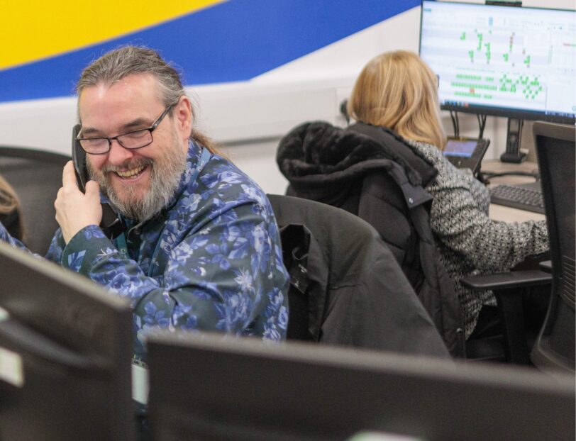 An image of a man at a desk in an office environment, answering a phone call.