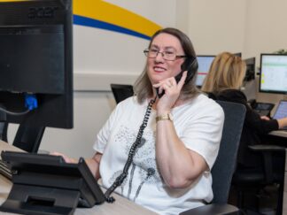 An image of a woman at a desk in an office environment, answering a phone call.