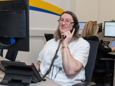 An image of a woman at a desk in an office environment, answering a phone call.