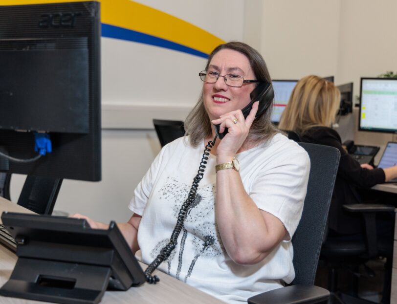 An image of a woman at a desk in an office environment, answering a phone call.