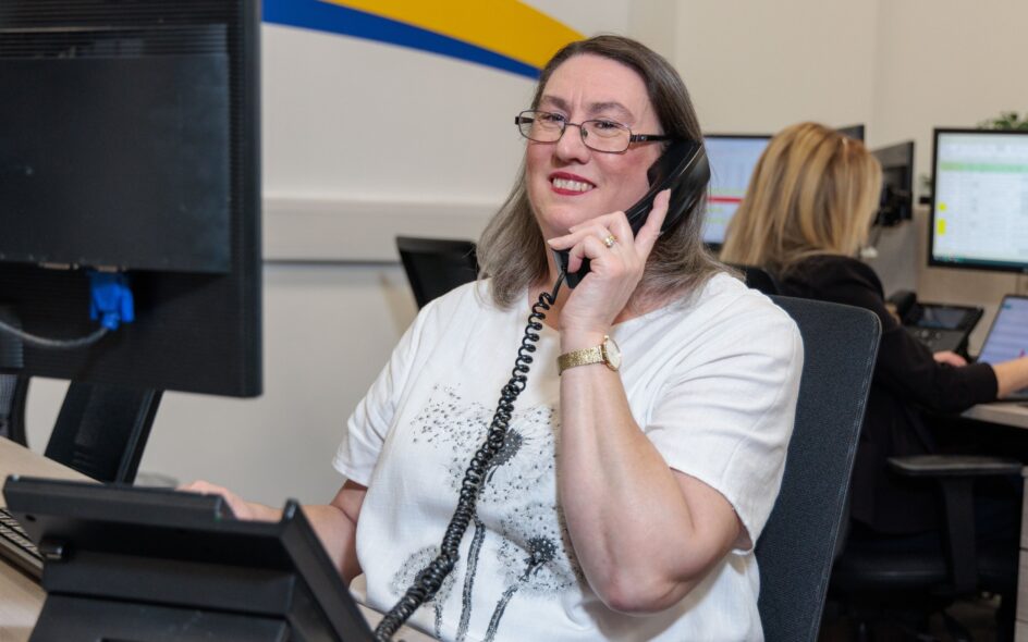 An image of a woman at a desk in an office environment, answering a phone call.