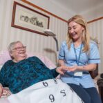 Image of a Care Assistant and an elderly lady in a home setting, holding hands.
