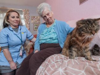 Image of a Care Assistant and an elderly lady, sat on a couch whilst petting a cat.