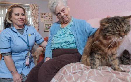 Image of a Care Assistant and an elderly lady, sat on a couch whilst petting a cat.