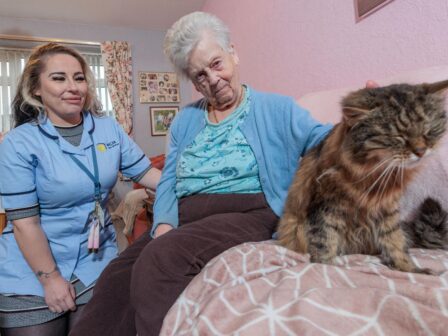 Image of a Care Assistant and an elderly lady, sat on a couch whilst petting a cat.