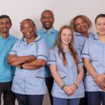 A group of 5 Care Assistants against a white wall.