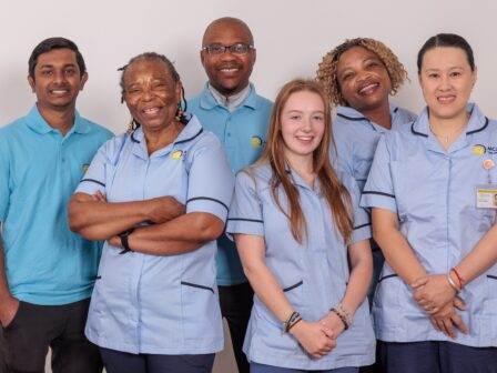 A group of 5 Care Assistants against a white wall.