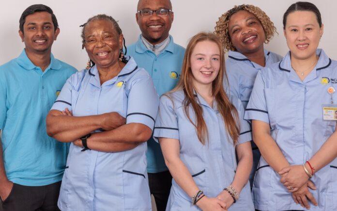 A group of 5 Care Assistants against a white wall.