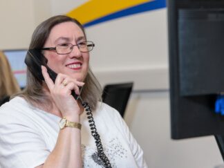 An image of a woman at a desk in an office environment, smiling and answering a phone call. help the best home care provider