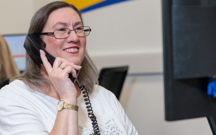 An image of a woman at a desk in an office environment, answering a phone call.