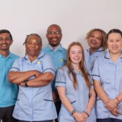 A group of 5 Care Assistants against a white wall.