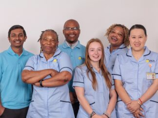 A group of 5 Care Assistants against a white wall.