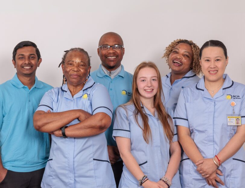 A group of 5 Care Assistants against a white wall.