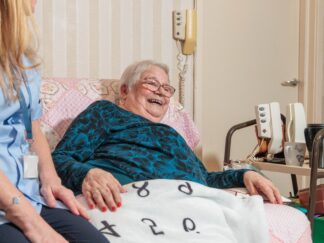 Image of a Care Assistant and an elderly lady in a home setting, holding hands. Domiciliary care
