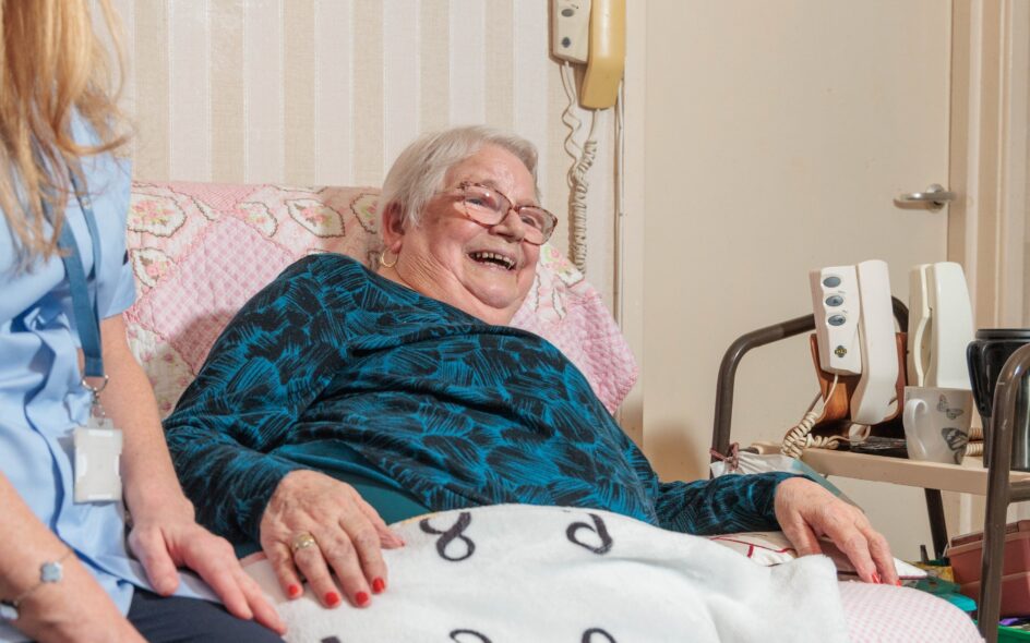 Image of a Care Assistant and an elderly lady in a home setting, holding hands. Domiciliary care