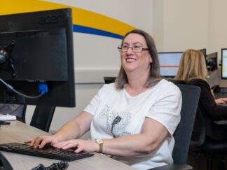 An image of a woman at a desk in an office environment, looking at her computer and typing.