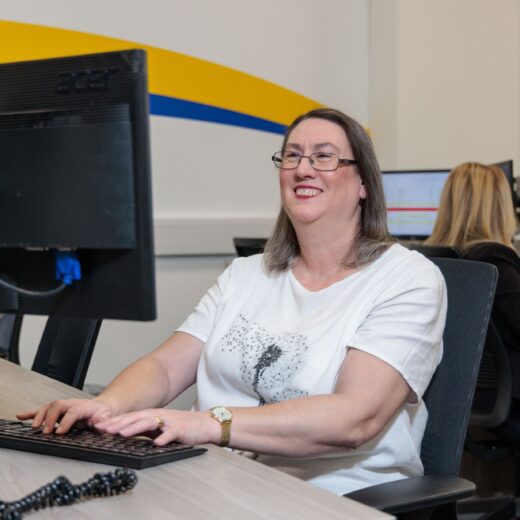 An image of a woman at a desk in an office environment, answering a phone call.