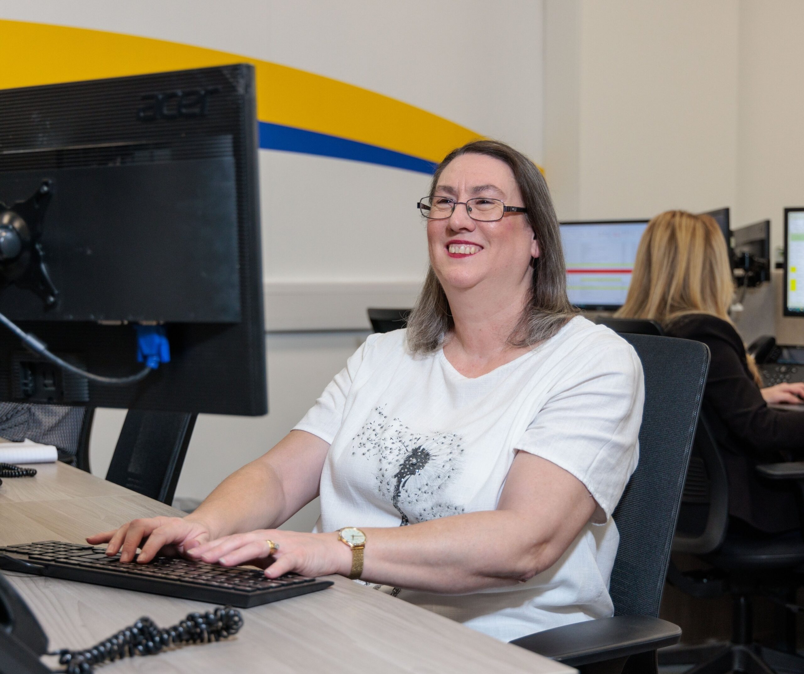 An image of a woman at a desk in an office environment, answering a phone call.