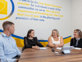 A man and 3 women in an office setting taking part in a meeting, laughing and smiling at each other. leading with care