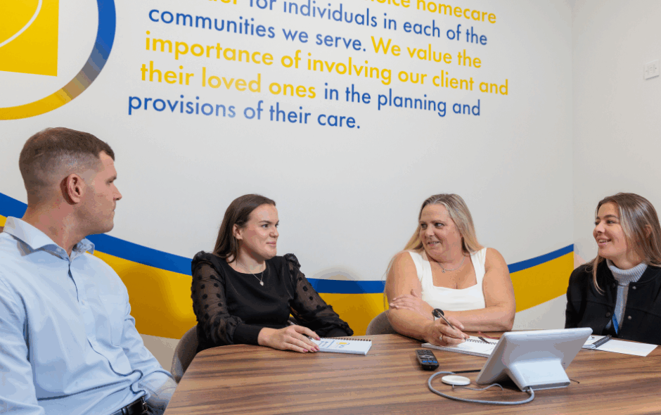 A man and 3 women in an office setting taking part in a meeting, laughing and smiling at each other. leading with care